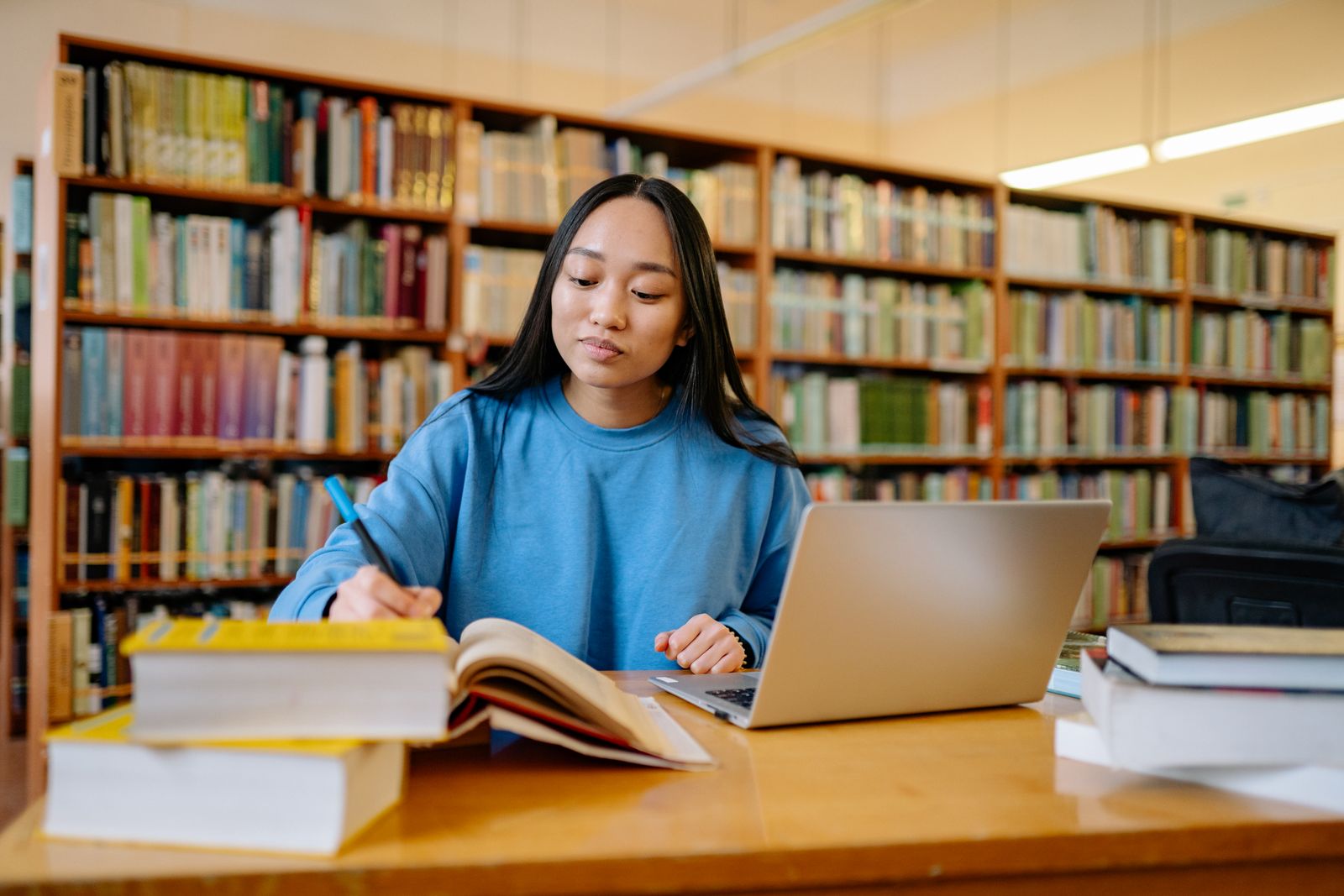 A graduate student working between a stack of textbooks and an open laptop in a university library